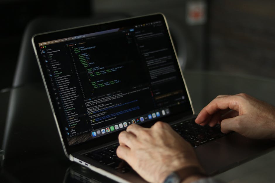 A person with a wristwatch is working on a laptop placed on a wooden surface, displaying a screen with lines of code. The environment appears to be indoors with adequate lighting, focusing on the user